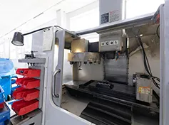 Close-up of a CNC machine in a workshop setting, featuring control panels, tool holders, and red storage bins for precision manufacturing components.